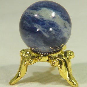 Può includere: Una sfera di pietra preziosa blu e bianca su un supporto in metallo dorato con tre gambe.