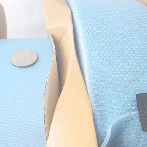 Può includere: Due rotoli di nastro autoagganciante blu chiaro, noto anche come Velcro, sono mostrati su bobine di cartone. Una moneta da 1 euro è posizionata su uno dei rotoli per mostrare la dimensione del nastro.