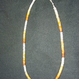 May include: A necklace made of small, round, orange, white, and brown beads. The necklace is strung on a silver chain.