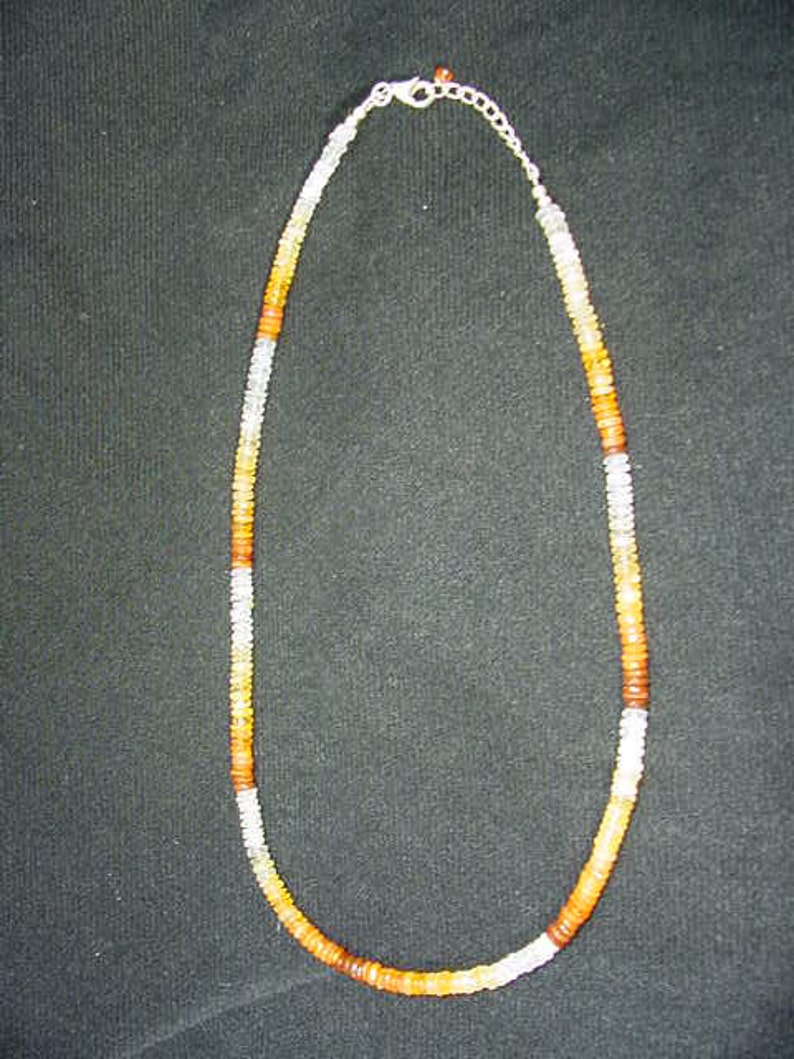 May include: A necklace made of small, round, orange, white, and brown beads. The necklace is strung on a silver chain.