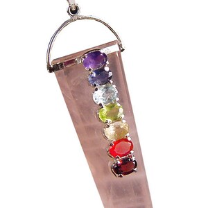 Könnte beinhalten: Eine silberne Kettenkette mit einem rosa Kristall-Anhänger. Der Anhänger hat sieben kleine Edelsteine in verschiedenen Farben, die die sieben Chakren repräsentieren.