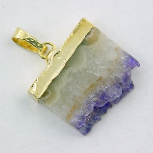 Può includere: Un ciondolo placcato oro con un cristallo di ametista naturale con un bordo ruvido e irregolare. Il cristallo è di colore viola chiaro e ha un centro bianco e nuvoloso.
