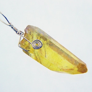 May include: A yellow crystal pendant with a silver wire wrap. The crystal is faceted and has a pointed tip.