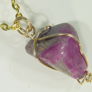 May include: A gold chain necklace with a pink and gray gemstone pendant wrapped in gold wire.