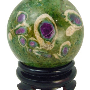 May include: Green and white sphere with pink and purple inclusions, polished and displayed on a black wooden stand.