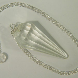 May include: A clear quartz crystal pendulum with a silver chain. The pendulum is shaped like a teardrop and has a faceted design.