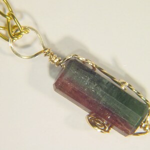 Può includere: Una collana con catena d'oro con un ciondolo con una pietra preziosa verde, rosa e nera avvolta in filo d'oro.