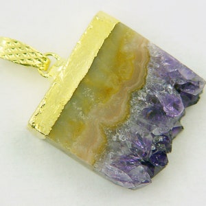 Può includere: Un ciondolo placcato oro con un cristallo di ametista naturale in colori viola e giallo. Il cristallo è tagliato in forma rettangolare e ha un bordo grezzo e naturale.