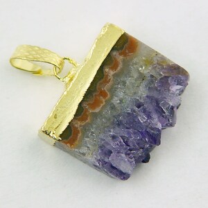 Può includere: Un ciondolo placcato oro con un cristallo di ametista viola con un bordo naturale grezzo. Il cristallo è incastonato in una cornice placcata oro.