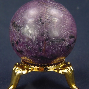 May include: A purple sphere with black flecks sits on a gold metal stand with three legs.