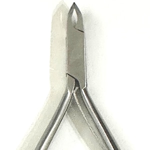 Puede incluir: Un alicate para cutículas de metal color plata con hojas afiladas y puntiagudas en el extremo y dos mangos largos y delgados que se extienden hacia abajo, diseñado para el corte preciso de la piel alrededor de las uñas de manos o pies.