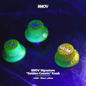 Puede incluir: Tres perillas de control de guitarra circulares con un acabado verde neón brillante y motas de purpurina dorada. Dos perillas están etiquetadas como TONE y una como VOLUME en letras oscuras. El texto 8NOV Signature Golden Cosmic Knob es visible.