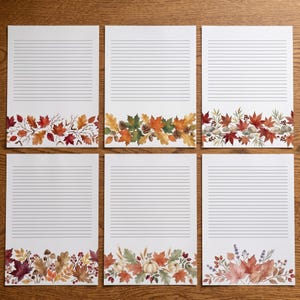 Puede incluir: Seis hojas de papel de carta blanco, cada una con líneas horizontales negras para escribir. La parte inferior de cada hoja está decorada con una ilustración única en acuarela de elementos otoñales, incluyendo hojas de arce, bellotas, calabazas y bayas.