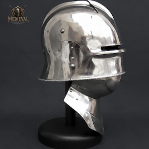 May include: A polished silver-colored metal sallet helmet with a horizontal eye slit and a rounded crown. The helmet features visible rivets along the side and a rope-like trim detail. The text MEDIEVAL ARMOR HUB is visible in the top left corner.