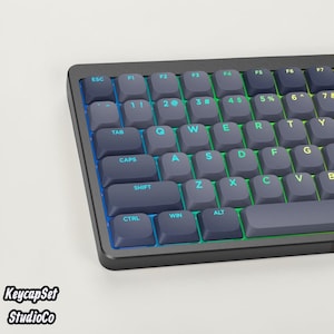 May include: A mechanical keyboard featuring dark grey keycaps with bright cyan and yellow backlit lettering. The keys include standard QWERTY layout markings such as ESC, TAB, CAPS, SHIFT, CTRL, WIN, and ALT, with a vibrant light glow between keys.