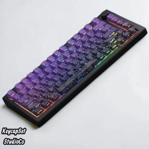 May include: A black mechanical keyboard featuring purple keycaps with a white topographic map pattern. The keyboard has a compact layout with a rotary knob in the top right corner and integrated RGB lighting that glows beneath the keys.
