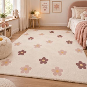 May include: A rectangular area rug with a cream-coloured background featuring a repeating pattern of five-petalled flowers in shades of dusty pink, dark mauve, and yellow. The rug has a soft, textured pile and covers the floor in a bedroom setting.