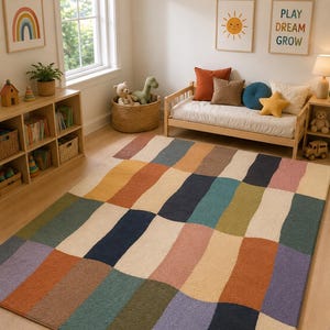 Könnte beinhalten: Ein rechteckiger Teppich mit einem sich wiederholenden Muster aus wellenförmigen, vertikalen Streifen in einer Palette gedämpfter Töne wie Terrakotta, Marineblau, Salbeigrün, Creme, Altrosa und Lavendel mit einer strukturierten Oberfläche.