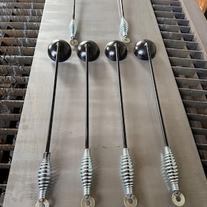 May include: Six metal tools with long black rods, each featuring a smooth black spherical head at one end and a silver-colored coiled spring handle at the other. Each handle terminates in a flat, circular silver washer with a central hole.