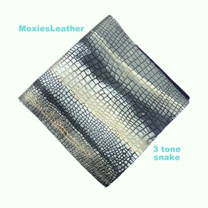 May include: A close-up of a piece of black, silver, and gold snakeskin leather. The leather has a textured pattern and is labelled "3 tone snake".