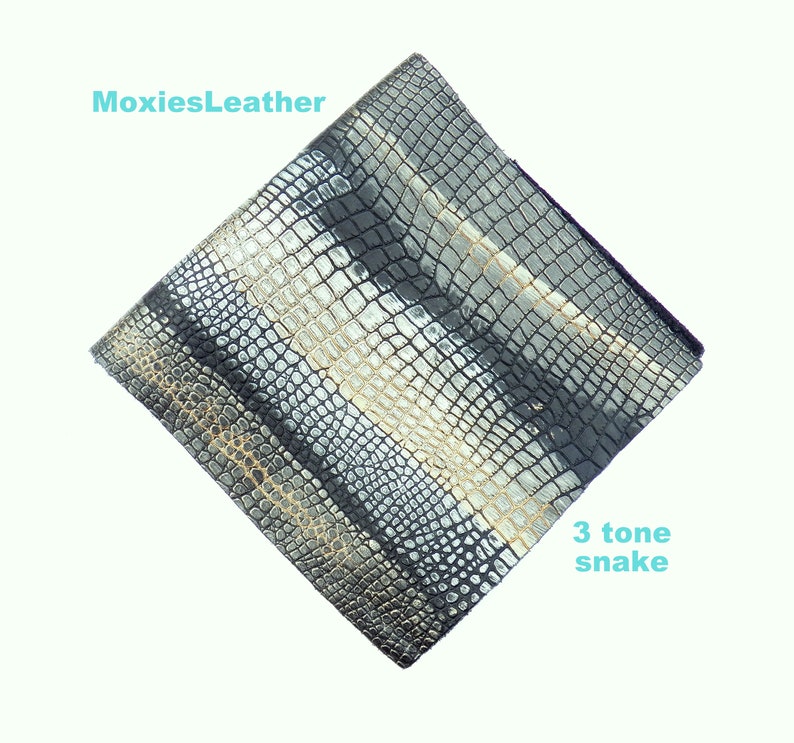 May include: A close-up of a piece of black, silver, and gold snakeskin leather. The leather has a textured pattern and is labelled "3 tone snake".