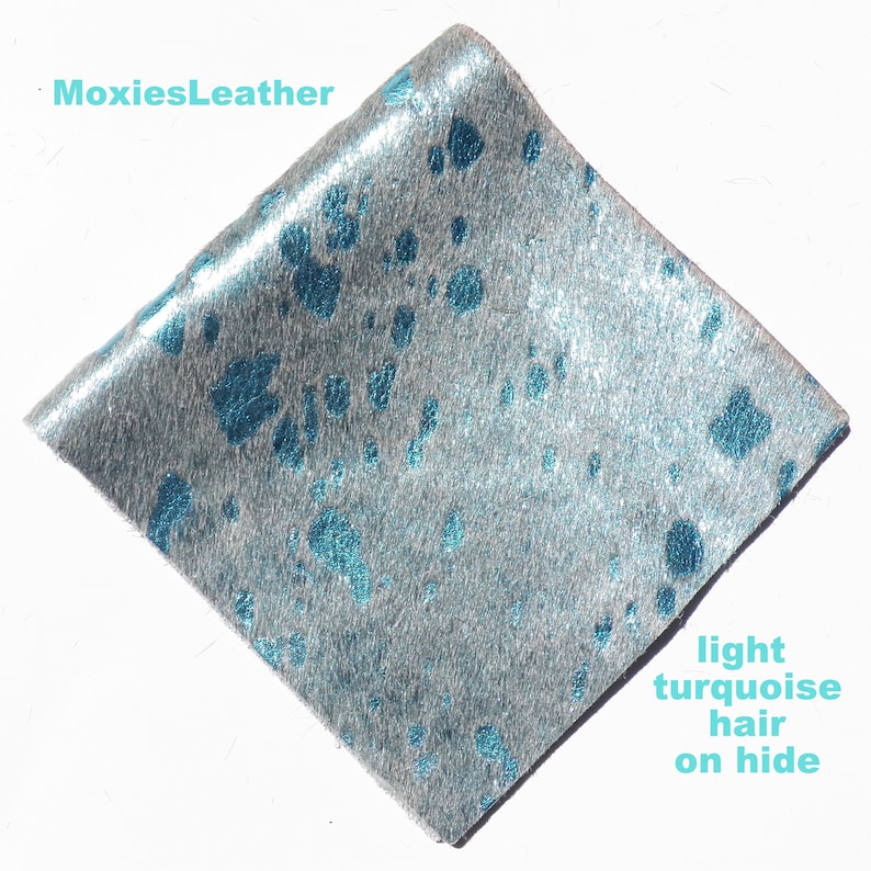 May include: A close-up of a piece of light turquoise cowhide leather with a silver metallic finish. The leather has a soft, fuzzy texture and is perfect for crafting.