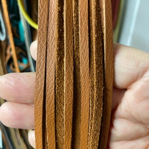 May include: A bundle of brown leather strips, each with a suede-like texture on one side. The strips are arranged vertically and are approximately 1.2 cm wide.