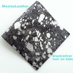 May include: A close-up of a black and silver cowhide leather with a diamond shape. The leather has a black base with silver spots.
