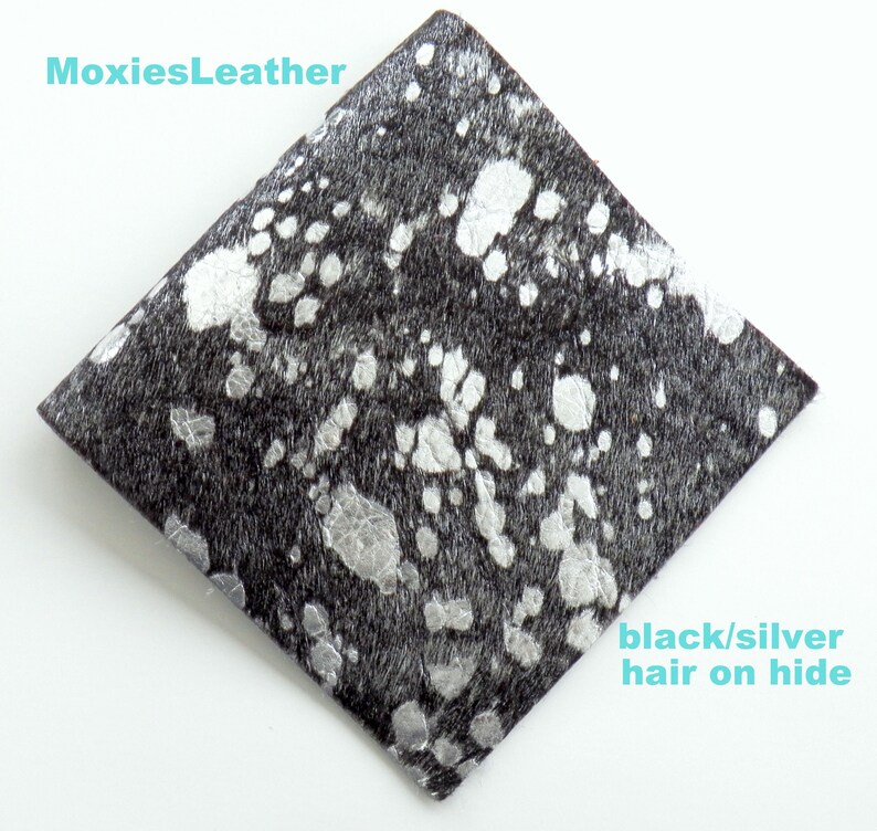 May include: A close-up of a black and silver cowhide leather with a diamond shape. The leather has a black base with silver spots.