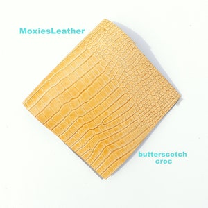 May include: Butterscotch colored crocodile embossed leather sheet.  The leather has a textured surface with a crocodile pattern.