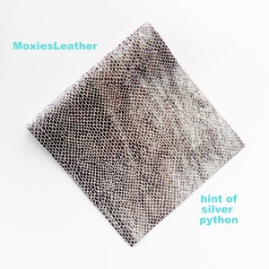 May include: A piece of silver python leather with a hint of grey. The leather has a textured, scaly pattern.