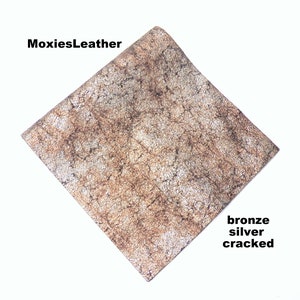 Puede incluir: Primer plano de un trozo de cuero agrietado con un acabado met&aacute;lico bronce y plateado. El cuero tiene un aspecto texturizado y envejecido. MoxiesLeather.