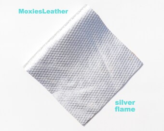 Może przedstawiać: Przybliżenie próbki srebrnej skóry o fakturowanej powierzchni. Próbka jest oznaczona jako "silver flame" i "MoxiesLeather".