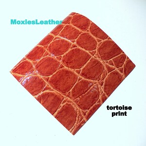 May include: A close-up of a piece of brown leather with a tortoise shell pattern. The leather has a glossy finish and is textured to resemble the skin of a reptile.