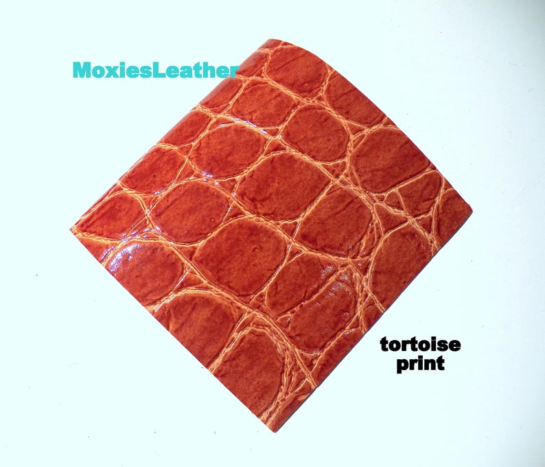 May include: A close-up of a piece of brown leather with a tortoise shell pattern. The leather has a glossy finish and is textured to resemble the skin of a reptile.