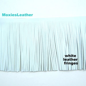 Könnte beinhalten: Weißes Lederfransenmaterial. Die Fransen bestehen aus langen, dünnen Streifen aus weißem Leder. Der Text "white leather fringes" ist im Bild sichtbar. Der Markenname "MoxiesLeather" ist ebenfalls sichtbar.