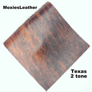 May include: A close-up of a piece of brown and black cowhide leather with a short, soft nap. The leather has a two-tone pattern and is labeled "Texas 2 tone".