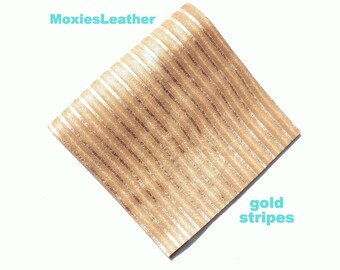 Może przedstawiać: Kawałek brązowej skóry ze złotymi paskami. Skóra ma ukośny wzór złotych pasków. Tekst "MoxiesLeather" znajduje się w lewym górnym rogu, a tekst "gold stripes" w prawym dolnym rogu.