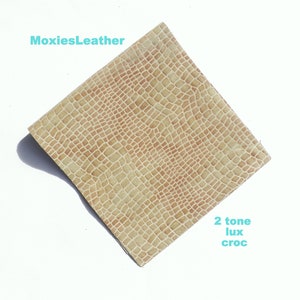 May include: A close-up of a two-tone beige and brown faux crocodile leather. The leather has a textured, embossed pattern. The text "MoxiesLeather" and "2 tone lux croc" are visible in the image.
