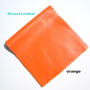 Könnte beinhalten: Ein Stück leuchtend orangefarbenes Leder. Das Leder ist glatt und hat einen leichten Glanz. Das Leder ist in der Mitte gefaltet und die Kanten sind sichtbar. Der Text "MoxiesLeather" befindet sich in der oberen linken Ecke des Bildes. Der Text "orange" befindet sich in der unteren rechten Ecke des Bildes.