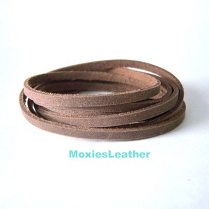 May include: A close-up of a brown leather cord, rolled up in a circle. The cord is about 1/4 inch wide and is made of a soft, supple leather.