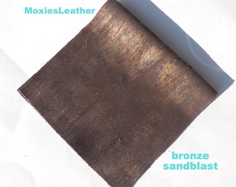 May include: A close-up of a piece of brown leather with a bronze sandblast finish. The leather has a textured surface and a subtle sheen.