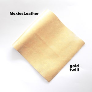 Puede incluir: Una muestra de tela de sarga dorada. La tela tiene una textura sutil y una sensaci&oacute;n suave y lujosa. La muestra est&aacute; etiquetada como "gold twill" y "MoxiesLeather".