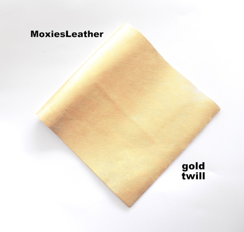 Puede incluir: Una muestra de tela de sarga dorada. La tela tiene una textura sutil y una sensaci&oacute;n suave y lujosa. La muestra est&aacute; etiquetada como "gold twill" y "MoxiesLeather".