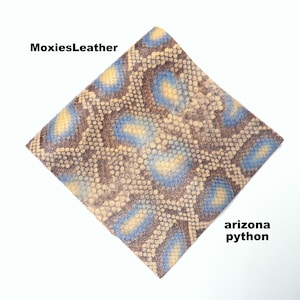 Puede incluir: Primer plano de un trozo de cuero de pitón de Arizona marrón y azul con un patrón texturizado. El cuero está etiquetado como "MoxiesLeather" y "arizona python".