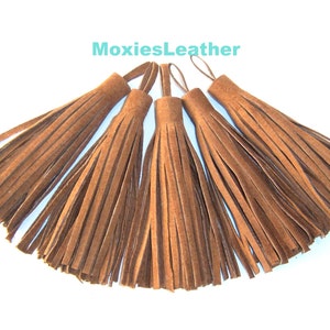 May include: Five brown suede tassels with a loop at the top. MoxiesLeather is printed in turquoise above the tassels.