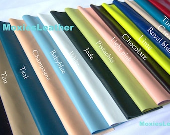 May include: A variety of leather swatches in different colors, including black, tan, teal, champagne, baby blue, white, jade, pistachio, light pink, chocolate, lime, royal blue, cream, turquoise, and red. The swatches are arranged in a row, with the darkest colors on the left and the lightest colors on the right. The text "MoxiesLeather" appears twice in the image.