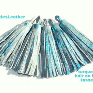May include: A set of six turquoise hair-on-hide tassels. The tassels are made of leather and have a fringed design. The tassels are a light blue color with a turquoise sheen.
