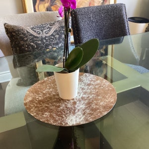 May include: A brown and white cowhide placemat with a white ceramic cup and a purple orchid plant in the center.