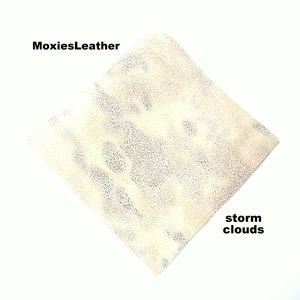 Puede incluir: Primer plano de un trozo de cuero blanco roto con una superficie texturizada. El cuero tiene un patr&oacute;n sutil de peque&ntilde;os puntos oscuros. El texto "MoxiesLeather" aparece en la esquina superior izquierda de la imagen. El texto "storm clouds" aparece en la esquina inferior derecha de la imagen.